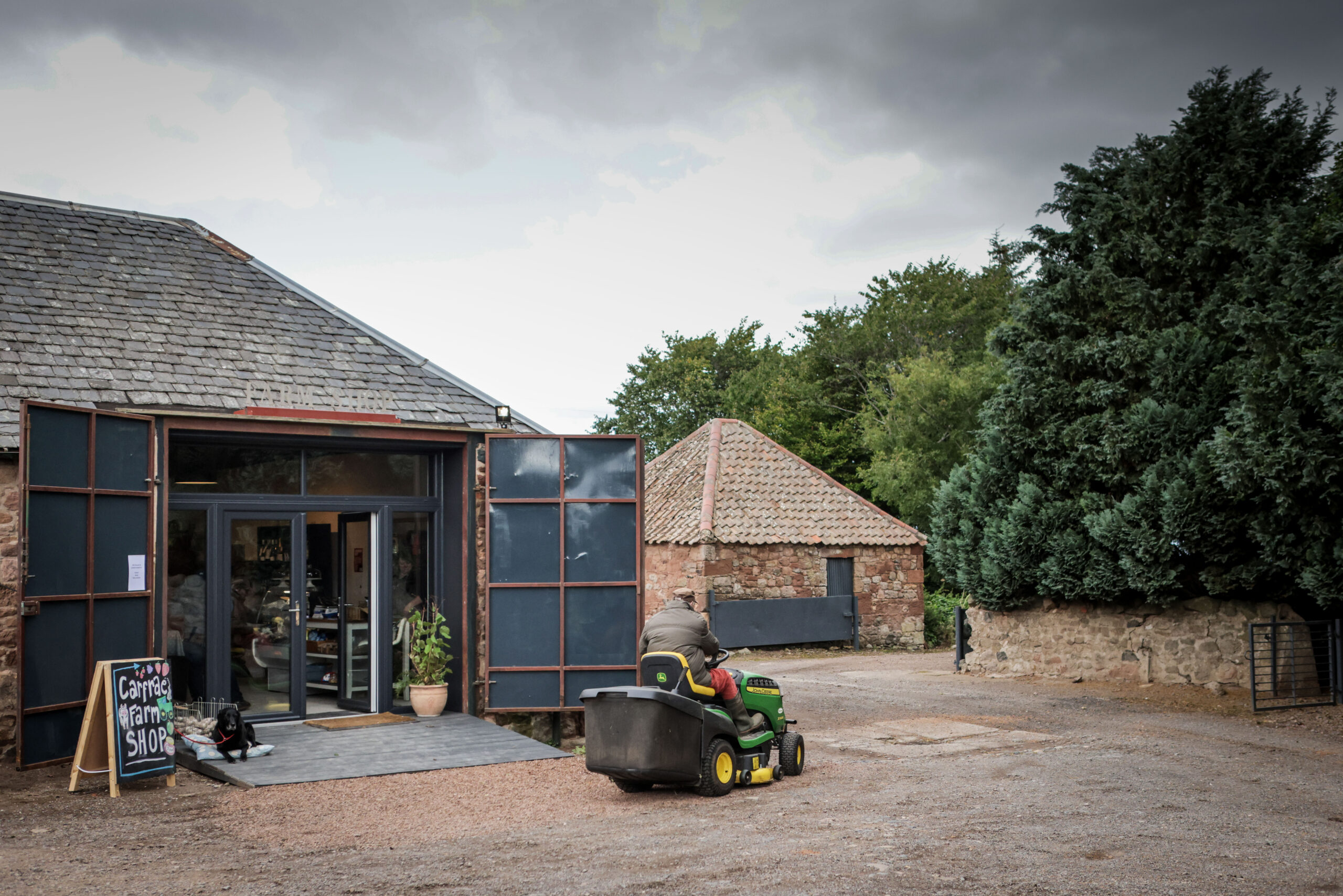 Carfrae Farm Shop exterior doors with Pip the black labrador and Hamish on a lawn mower